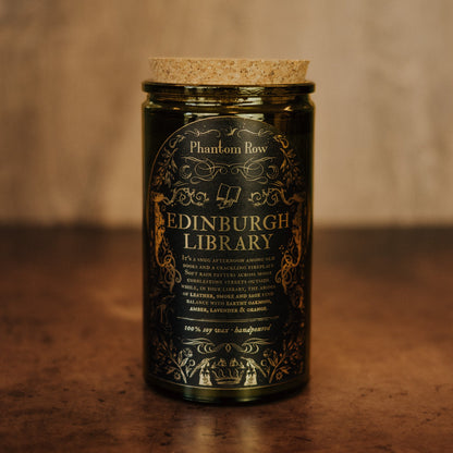 Candle jar labeled 'Edinburgh Library' by Phantom Row on a wooden surface with a blurred background.