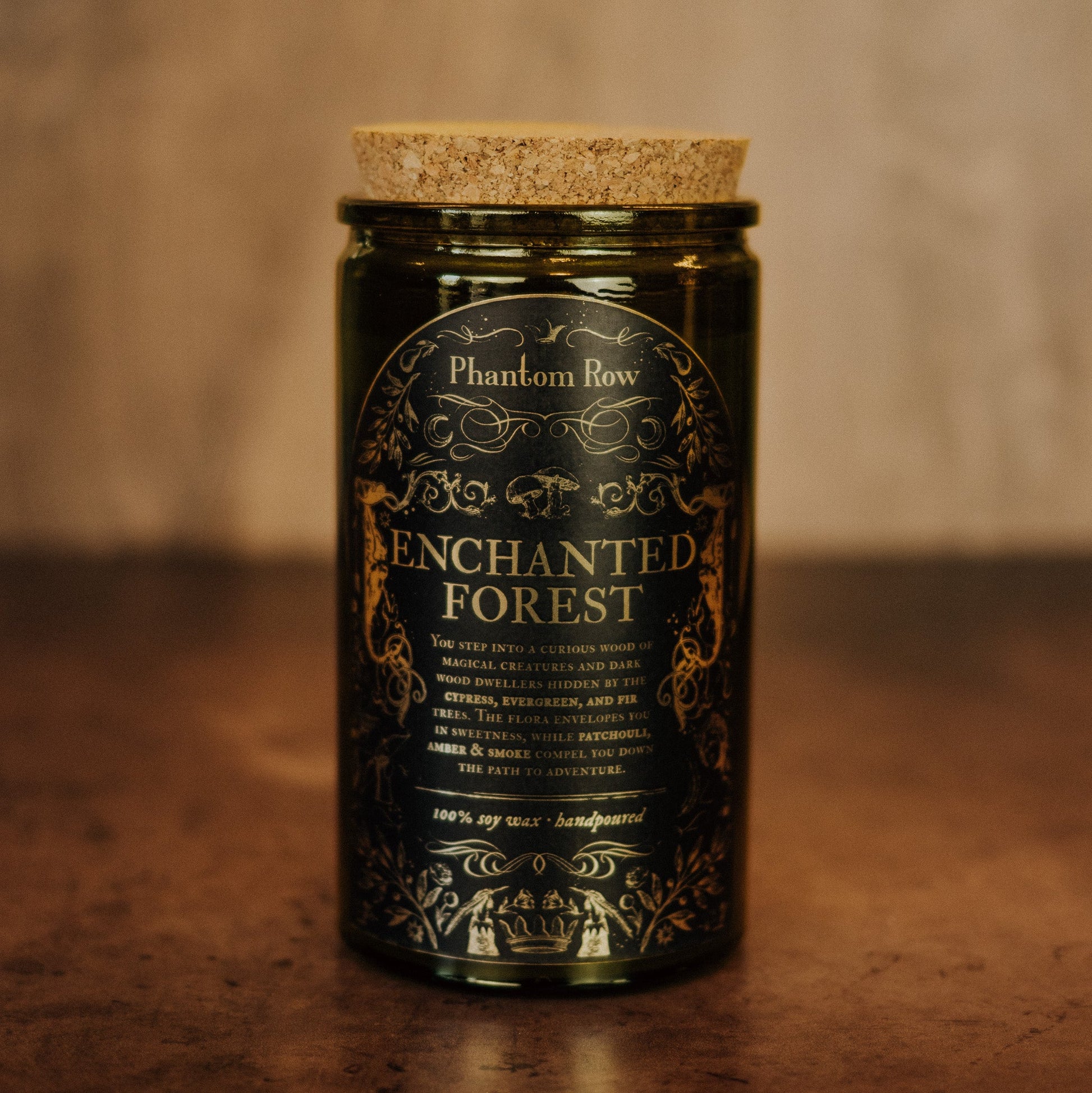 Candle jar labeled 'Enchanted Forest' by Phantom Row on a wooden surface with a blurred background.