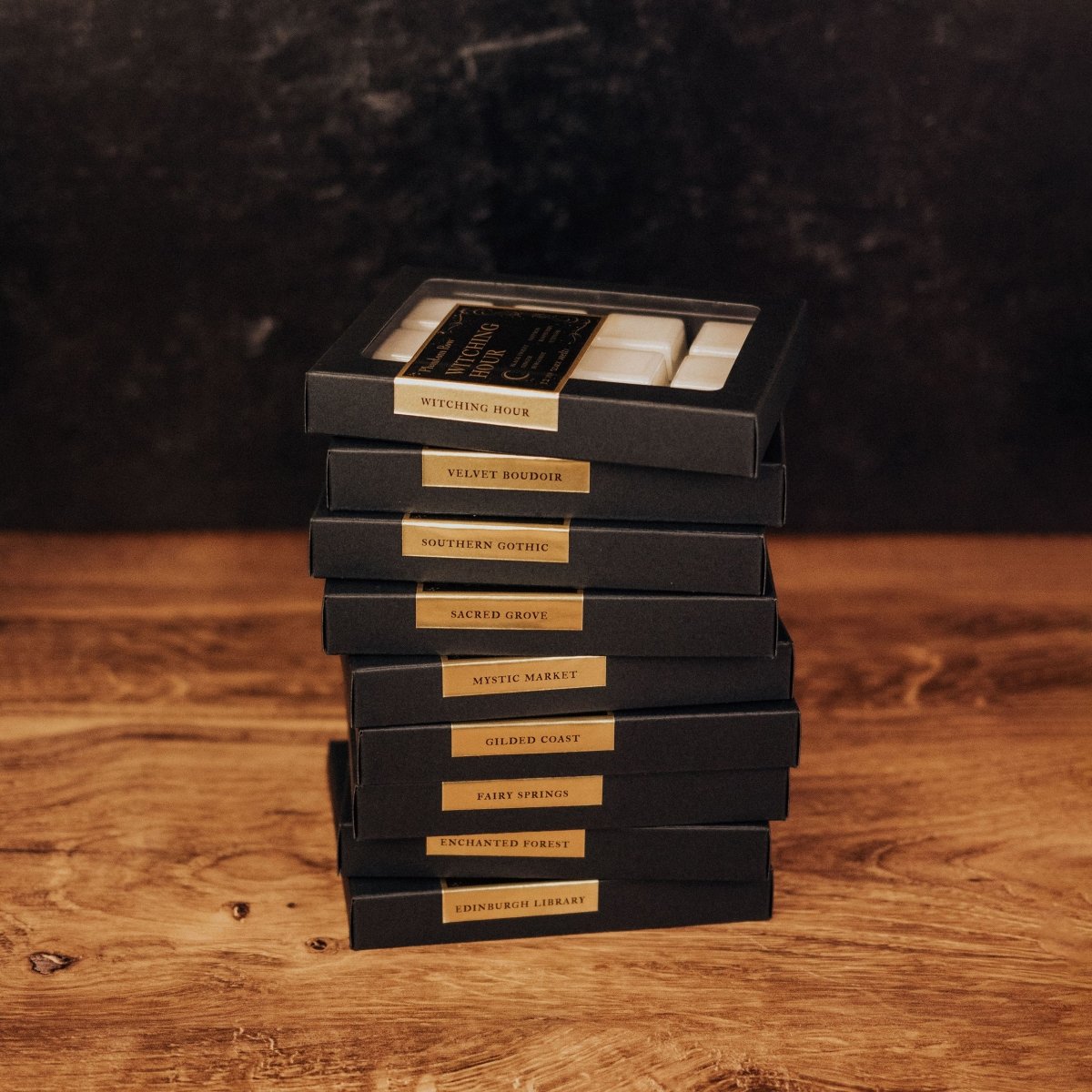 Stack of wax melts in black boxes with gold text on a wooden surface