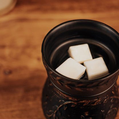 Black ceramic container with white wax melt cubes inside on a wooden surface