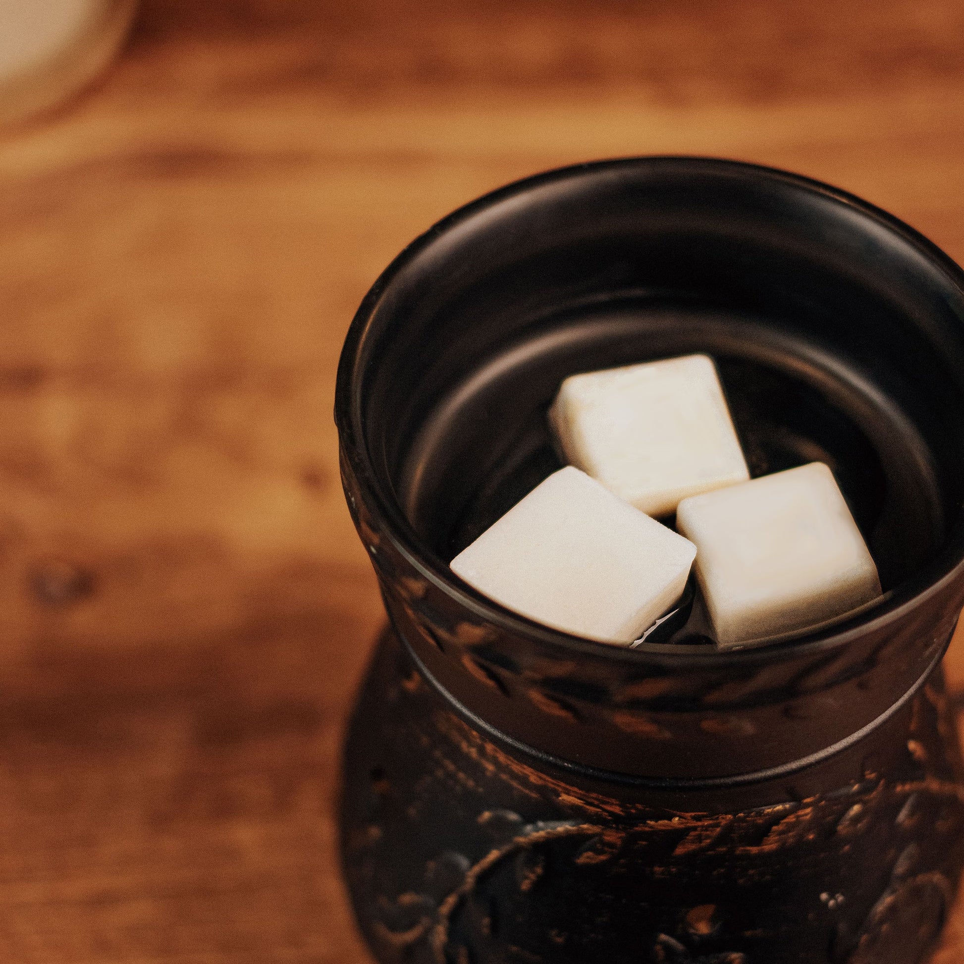 Black ceramic container with white wax melt cubes inside on a wooden surface