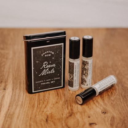 Room mist travel set with three bottles and a black tin on a wooden surface