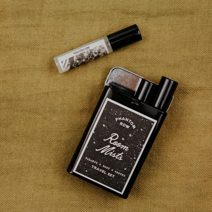 Black travel set of room mists with 'Phantom Row' branding on a textured brown surface